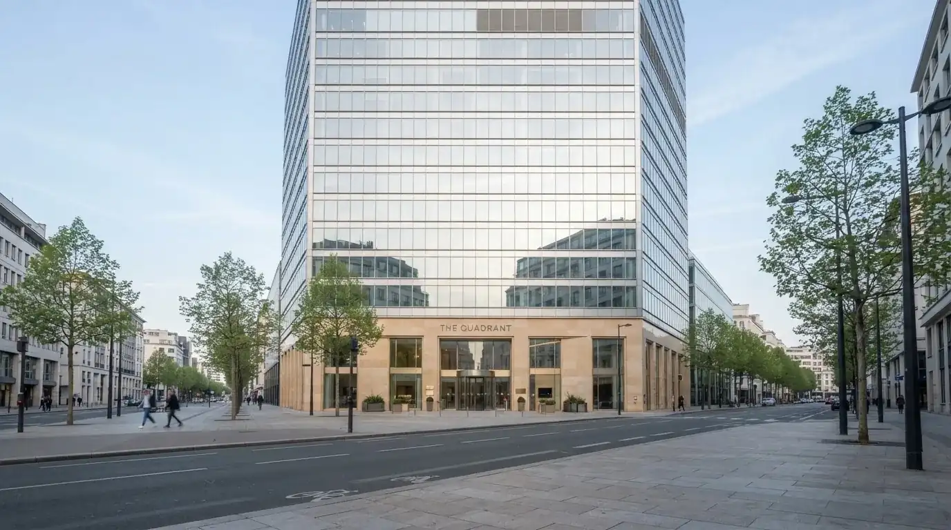 Un edificio de oficinas con fachada de cristal reflejando el cielo, fotografiado desde la acera de una calle ancha.